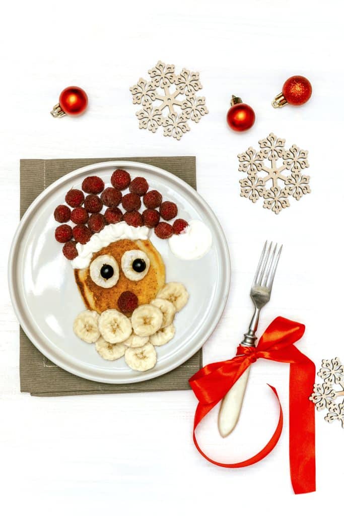 healthy christmas breakfast for kids pancake with banana and raspberries into a reindeer with santa hat